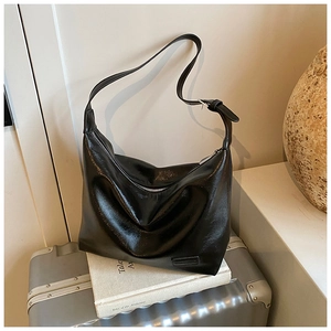 Detail of a shiny black faux leather crescent bag with adjustable strap on a vintage suitcase