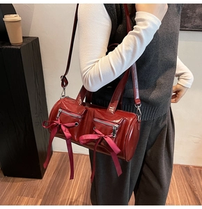 Détail du sac cylindre en cuir verni bordeaux avec poches et nœuds décoratifs