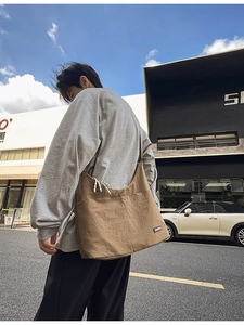 Large khaki canvas crossbody bag with drawstring detail shown in an urban street setting