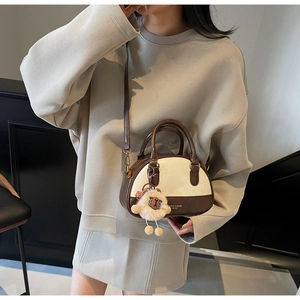 Brown and beige shell-shaped crossbody bag with a plush sheep charm shown on a model