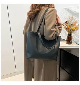 Detail of a black textured leather tote bag worn with a coat to show large capacity