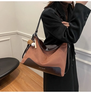 Detail of a brown suede tote bag with leather panels and baseball themed charms