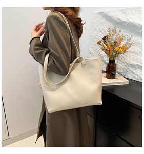 Lifestyle shot of large beige pebble leather tote bag worn with a brown blazer