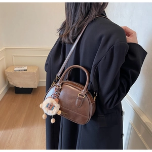 Close-up of retro dark brown shell bag with plush charm and golden metal hardware