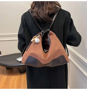 Detail of a brown suede hobo bag featuring a leather base and baseball themed charm