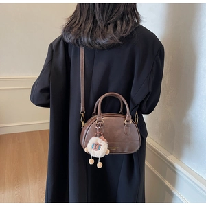Detail view of a brown leather boston bag with a cute white sheep charm and shoulder strap
