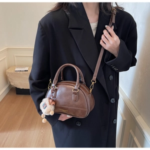 Brown vintage Boston bag with top handles, crossbody strap and plush bear charm detail
