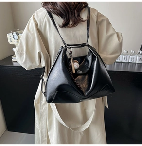 Detail of a large black glossy leather tote with baseball charm and woven rope accent