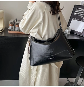 Detail of a large black glossy faux leather tote bag showing high-quality texture and brand logo