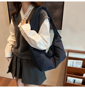 Detail of dark blue crescent dumpling bag with wide shoulder strap worn by a model