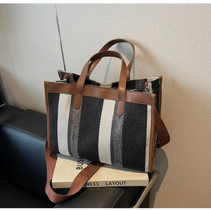 Detail of a large canvas tote with black and white stripes and brown leather trim handles