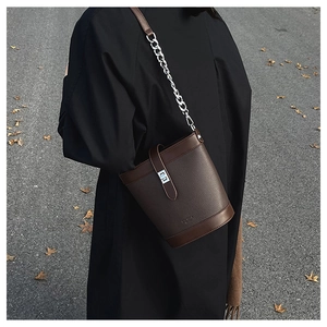 Detailed view of dark brown pebbled leather bucket bag with silver chain and lock