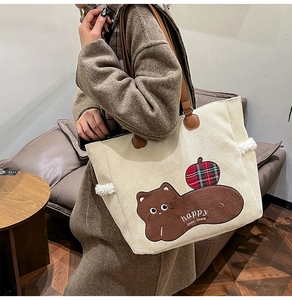 Model wearing a cream corduroy tote bag with cartoon embroidery in a cozy cafe
