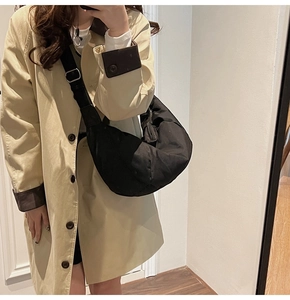 Detail of black crossbody crescent bag with wide adjustable strap worn on beige trench coat