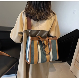 Close-up of striped canvas tote bag with brown leather handles and wide shoulder strap