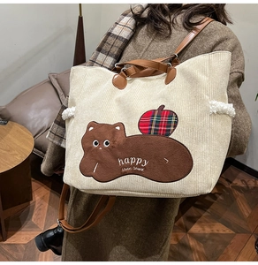 Detail of corduroy tote bag featuring plush bear embroidery and plaid apple patch detail