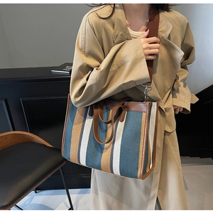 Detailed shot of striped canvas tote bag with leather handles and woven crossbody strap