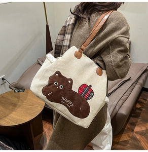 Detail of cream corduroy tote bag featuring bear embroidery and brown leather handles