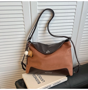 Detail of a two-tone brown tote bag with silver clasp and baseball charm on a leather sofa