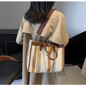 Detail of striped canvas tote bag with brown leather trim and wide fabric shoulder strap