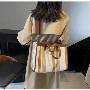 Rear view of model carrying a striped canvas tote bag with brown faux leather trim
