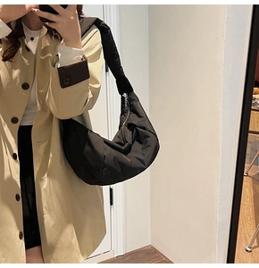 Detail of a black quilted crescent moon nylon bag worn with a beige trench coat