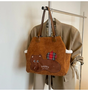Detailed view of brown corduroy tote with cartoon bear embroidery and leather handles