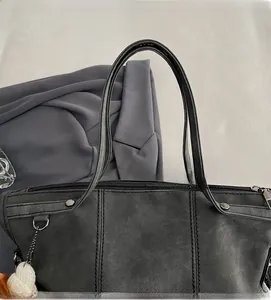 Detail of dark grey suede tote bag with silver studs and white pompom charm accessory