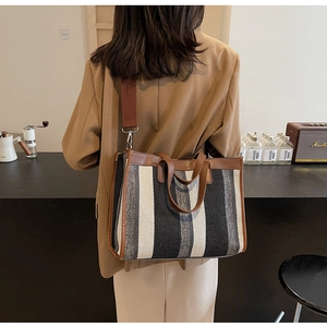 Back view of a model wearing a large striped canvas tote bag in a cafe setting