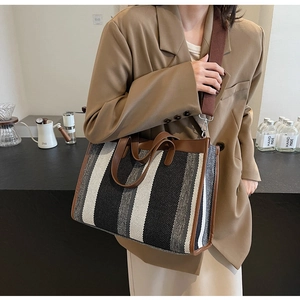 Detailed close-up of striped canvas tote bag with brown leather handles and wide shoulder strap
