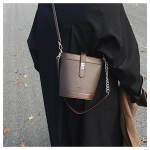 Detail of a brown bucket bag with lychee texture, metal magnetic buckle, and chain strap
