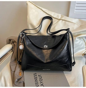 Detail of black glossy tote bag featuring a silver twist lock and baseball charm