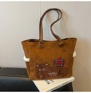 Close-up of corduroy tote bag with cat embroidery and leather straps in caramel