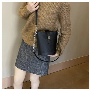 Detail of black bucket bag with lychee grain texture and gold metal buckle closure