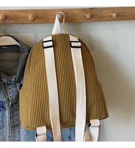 Detail view of mustard corduroy backpack with adjustable straps and side pockets on wooden hook