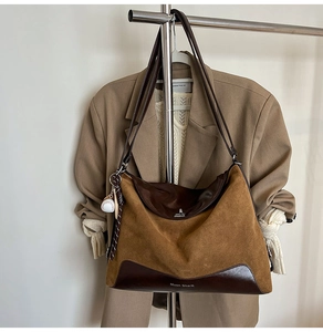 Detail of a brown leather tote bag with Muon Shark text and a baseball charm accessory