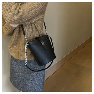 Detail of black pebbled leather bucket bag with gold lock and chain shoulder strap