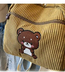 Detail of yellow corduroy backpack featuring bear embroidery and bear-shaped zipper pull