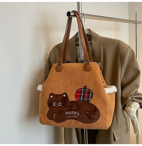 Detailed close-up of brown corduroy tote bag with plush animal embroidery and leather straps