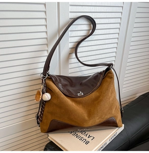 Detail of a brown suede tote bag with logo branding and a baseball glove charm accessory