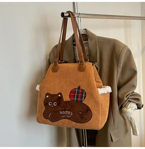 Close-up of yellow corduroy tote bag featuring cat embroidery and brown leather handle