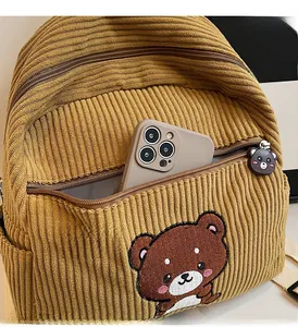 Detail of yellow corduroy backpack featuring bear embroidery and zipper pocket texture