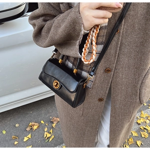 Detail of black leather crossbody bag with gold round lock and woven handle shown on model