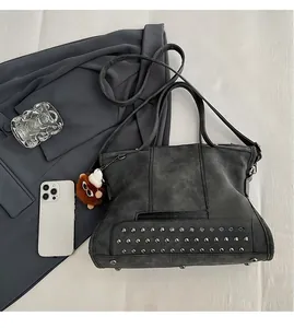 Macro detail of dark grey rivet tote bag with fringe accents and plush charm