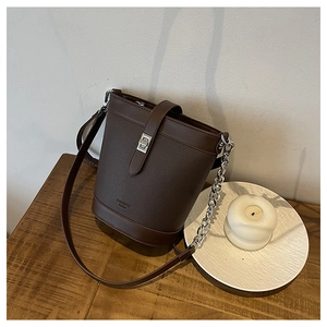 Detail of dark brown leather bucket bag with silver clasp and chain strap on wooden table