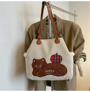 Detail of corduroy tote bag featuring animal patch, apple embroidery and brown PU handles