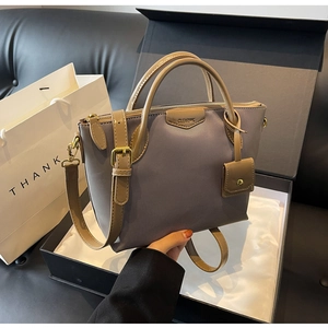 Detail of grey-purple textured handbag with brown leather straps in a gift box