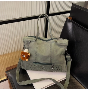 Detail of gray-green tote bag featuring silver rivet studs and a plush monster charm