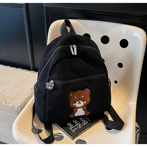 Close-up of black corduroy backpack featuring a cute bear patch and striped texture detail
