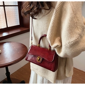 Detailed view of glossy burgundy leather surface and golden ring swivel lock on a bag